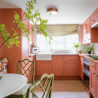 kitchen with coral cabinets, green dining chairs, window with patterned curtain and green plant