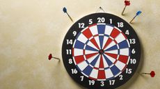 A dartboard surrounded by darts stuck in the wall rather than the dartboard.
