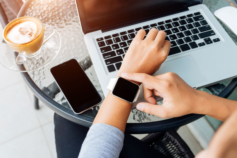 An Apple Watch, an iPhone and a MacBook in a cafe.