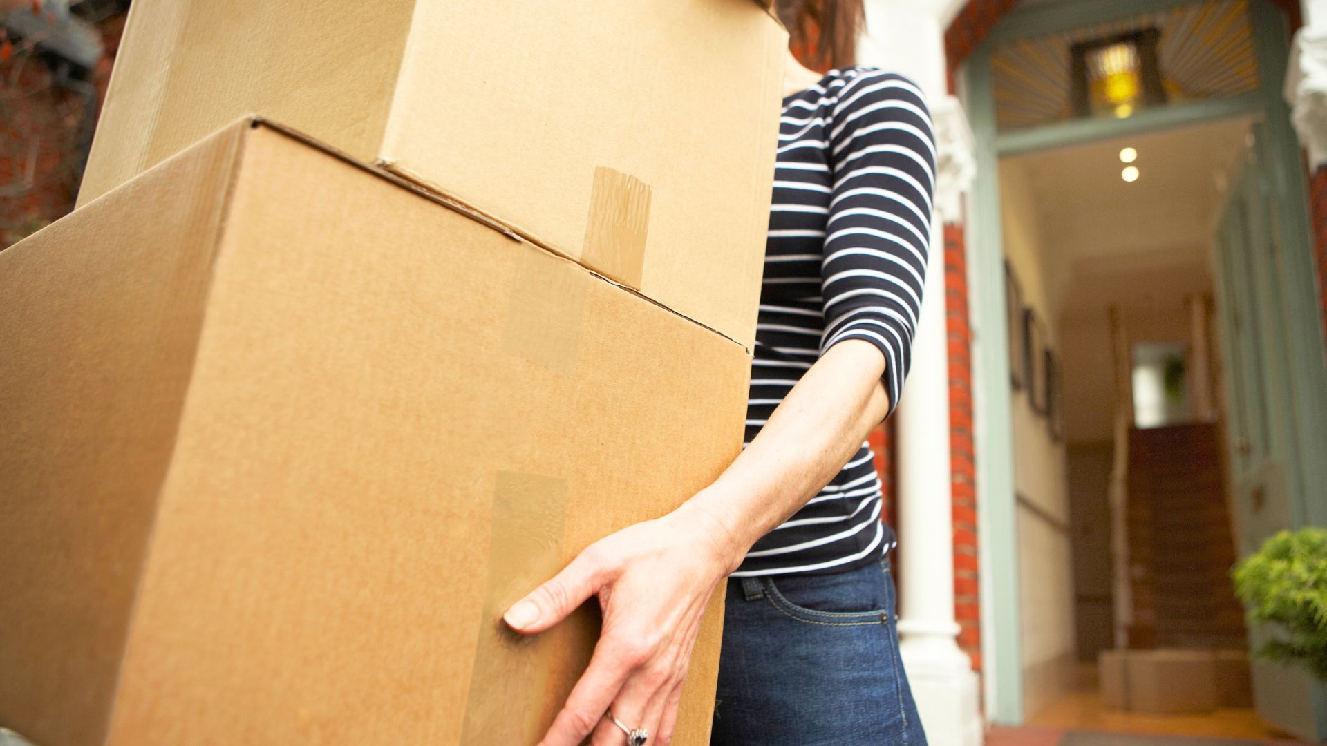 Woman carrying two cardboard boxes out of the house