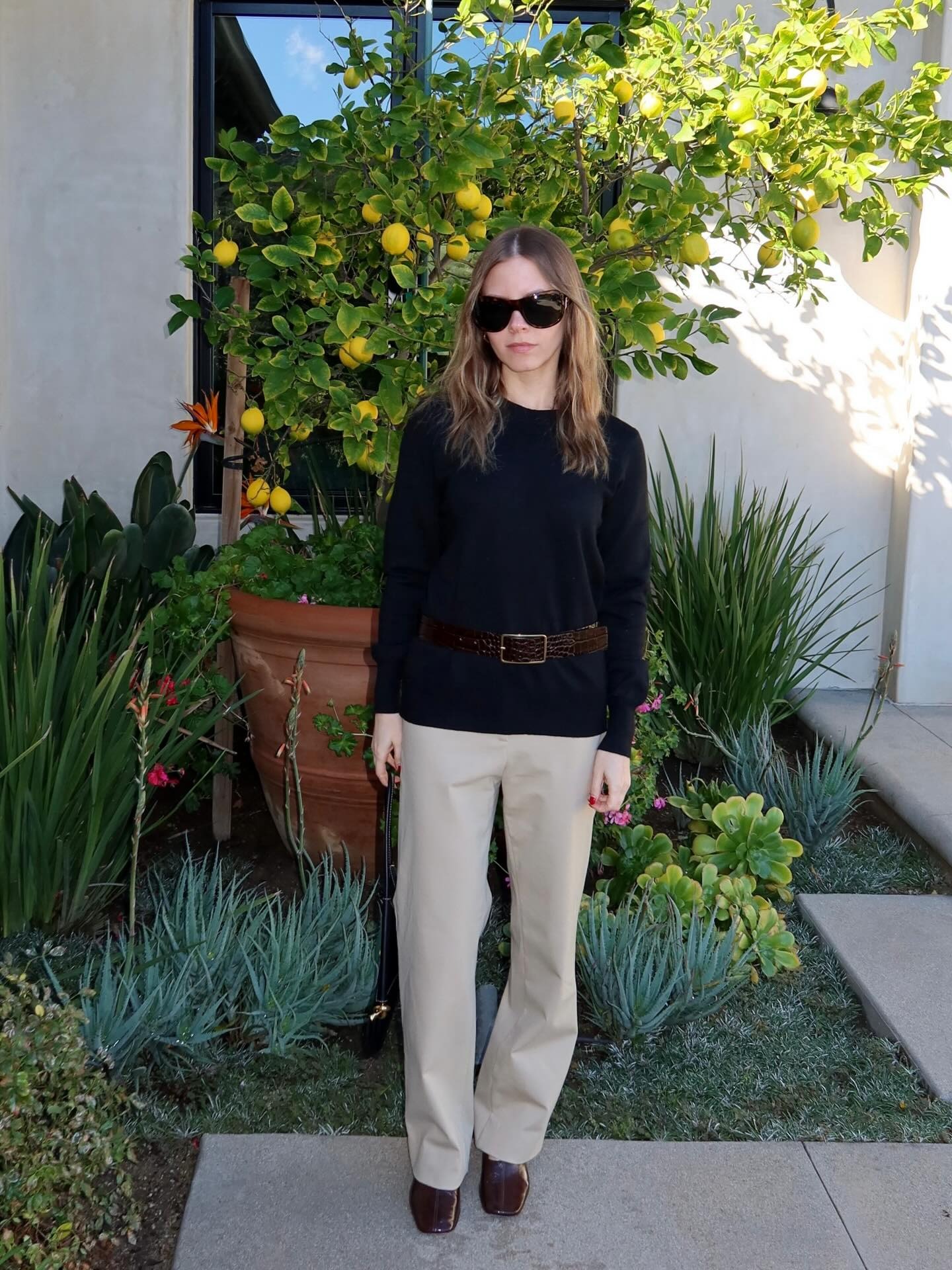 Nikki Chwatt wearing a black top, khaki pants, and burgundy Reformation Inez high-vamp pumps.