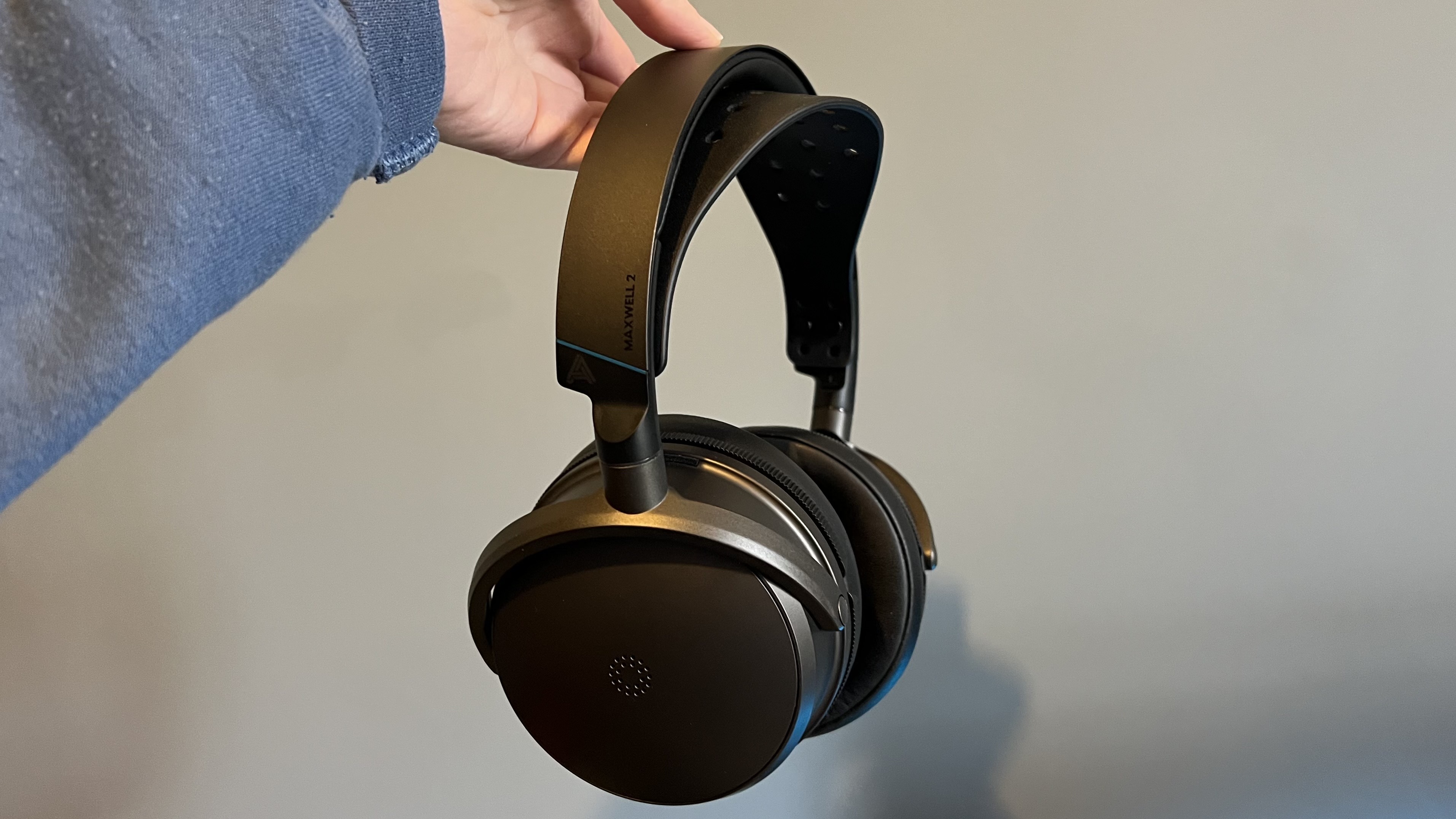 Audeze Maxwell 2 being held by the headstrap in front of a blue wall