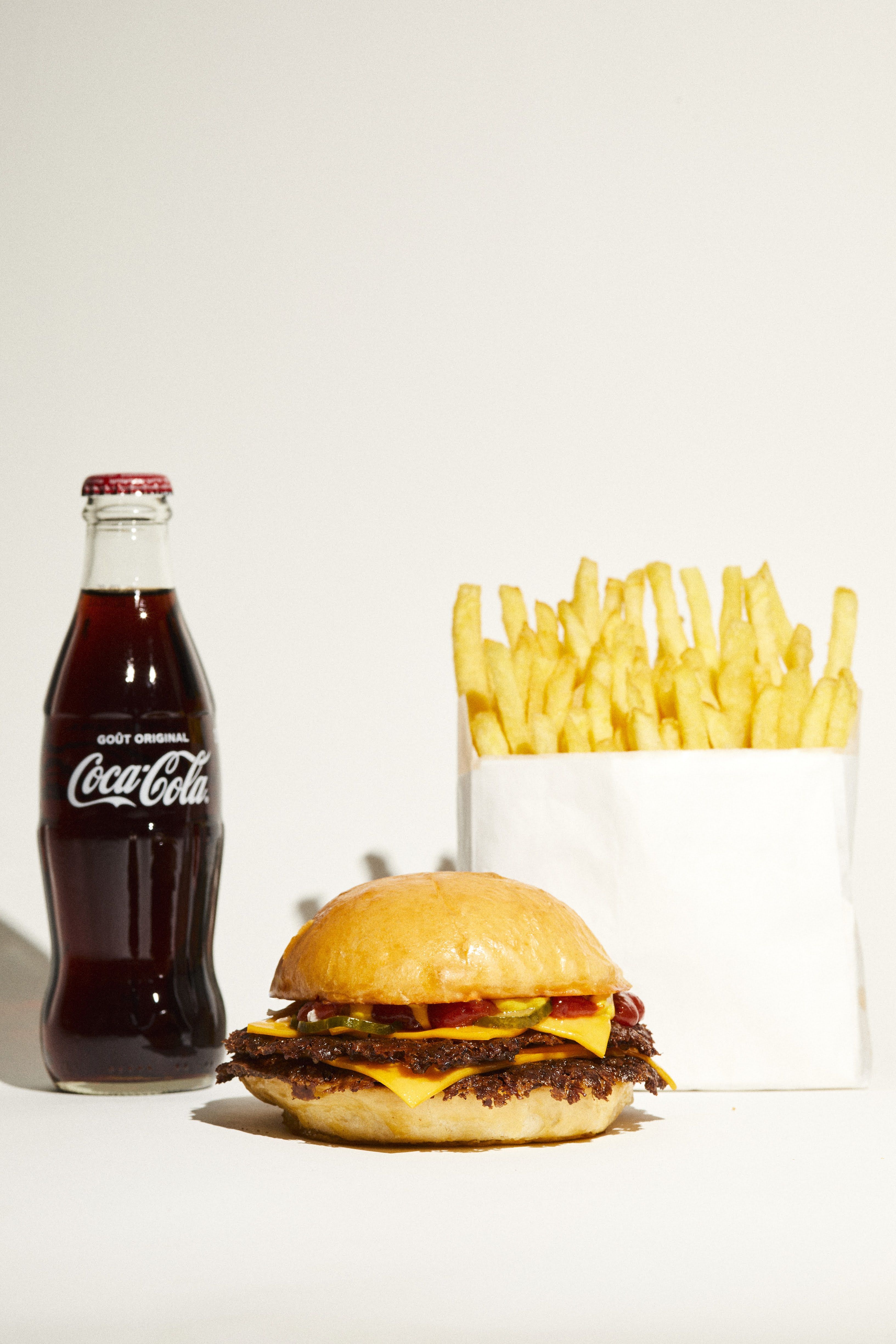 A smash burger sits between a bottled coke and fries against a white background.