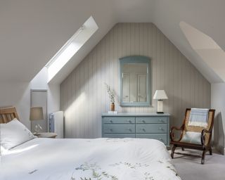 Guest bedroom with panelled end wall with chest of drawers, double bed, chair and roof windows