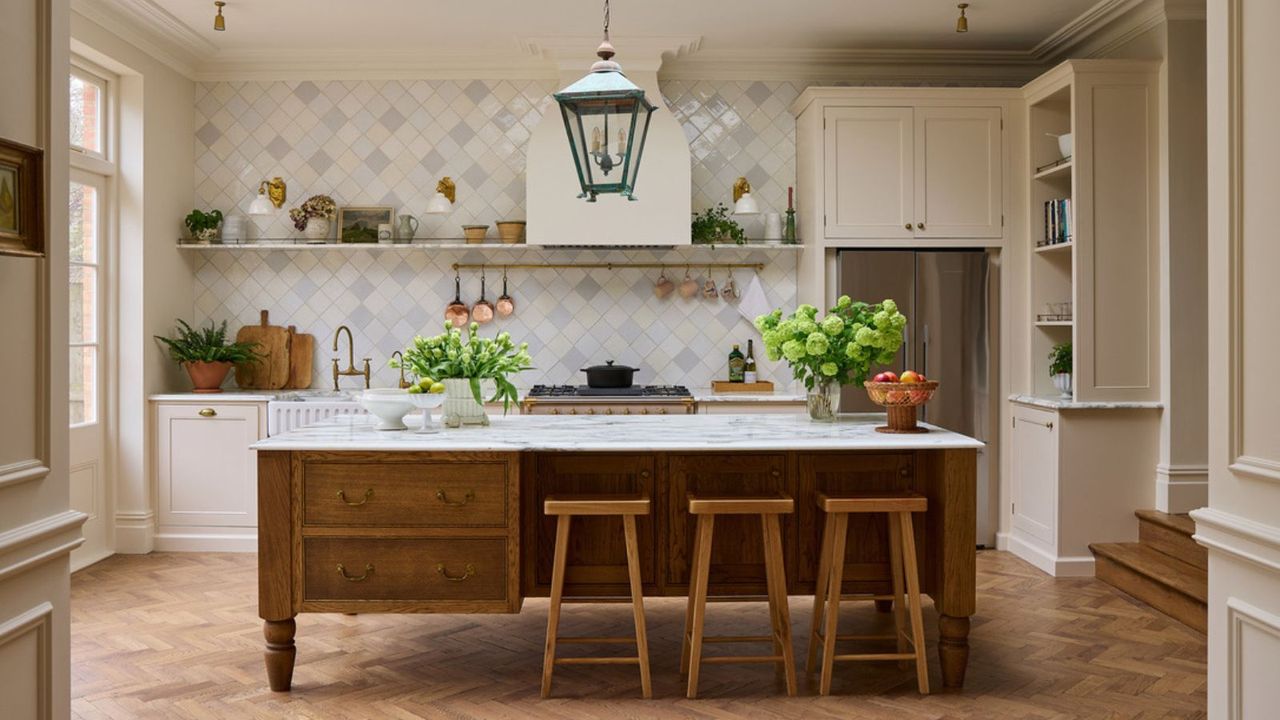 A warm neutral kitchen with cream cabinets, a wooden island, marble countertops, and a tiled backsplash