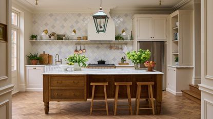 A warm neutral kitchen with cream cabinets, a wooden island, marble countertops, and a tiled backsplash