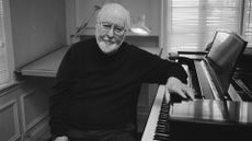 Legendary composer John Williams sitting at a piano as he looks into the camera in Music By John Williams