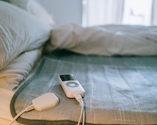 Blue heating pad on bed with soft lighting and white controller in view