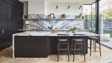 A modern kitchen with a large island, a marble countertop, and a book-matched marble backsplash