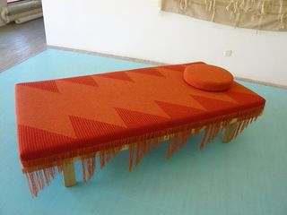 Wooden daybed with red and orange zig-zag design textile, round orange pillow, and fringes