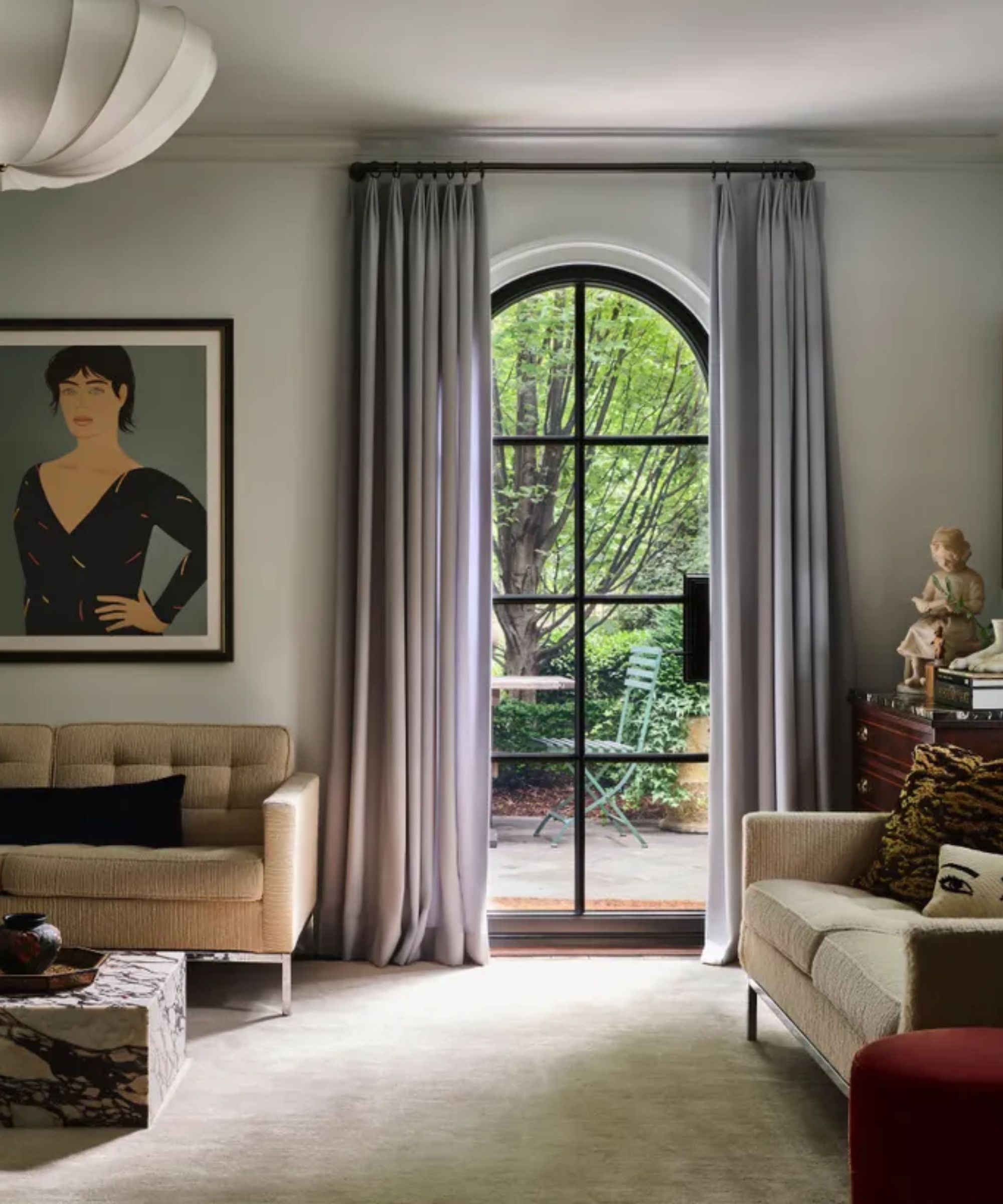 Contemporary living room with arch doorway, gray curtains, cream sofas and rug, artwork on wall