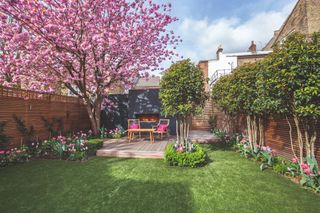 a cute backyard with green lawn, deck and blossoming plum tree, and wood fences