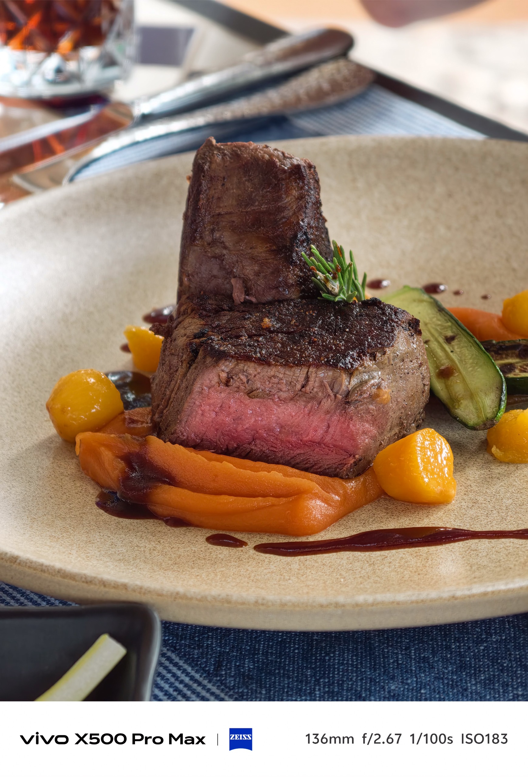 Thick grilled steak served with orange puree, vegetables, and sauce on a ceramic plate.