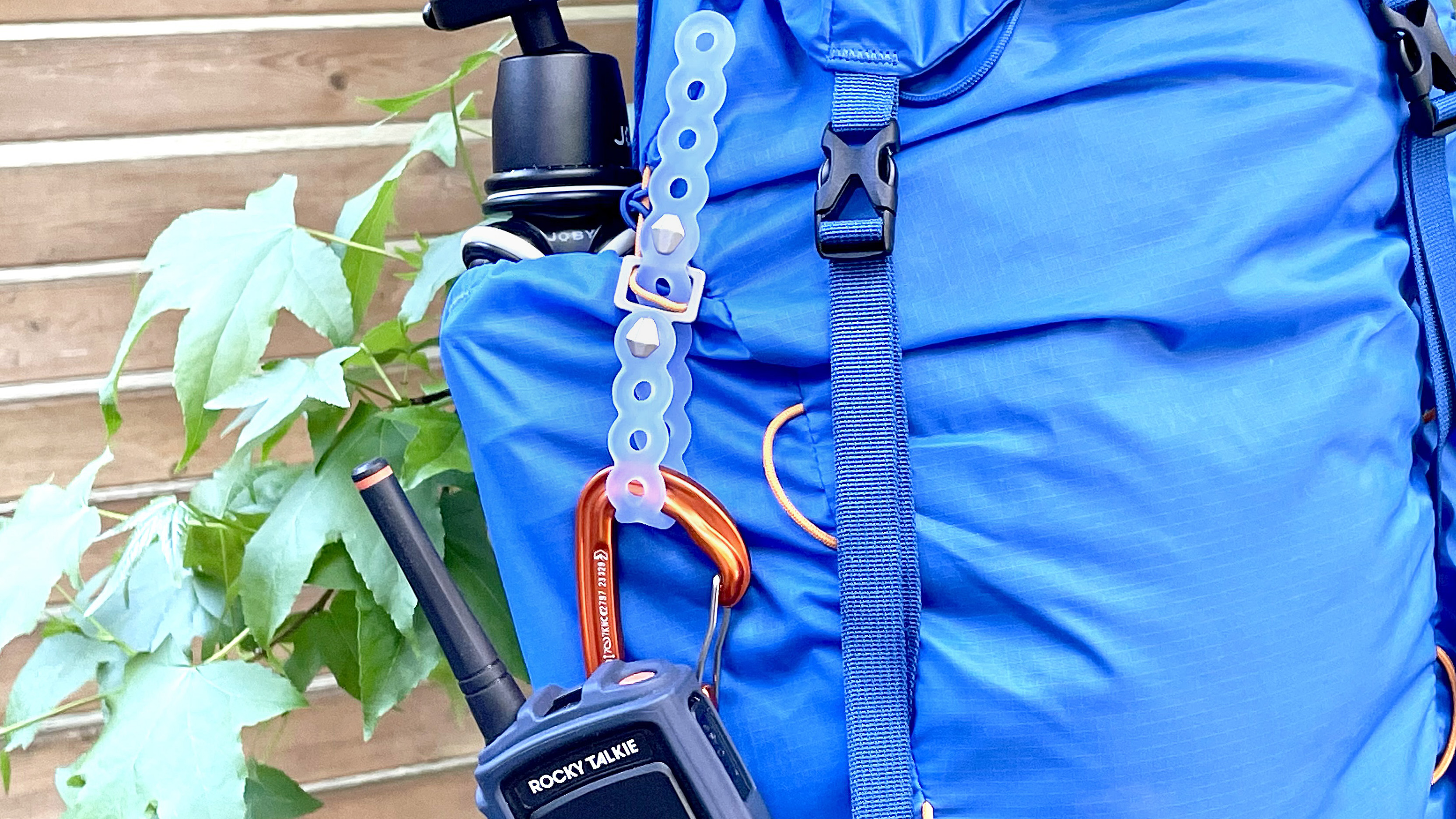 A close-up of the Infinity modular strap holding a walkie talkie to a blue hiking backpack