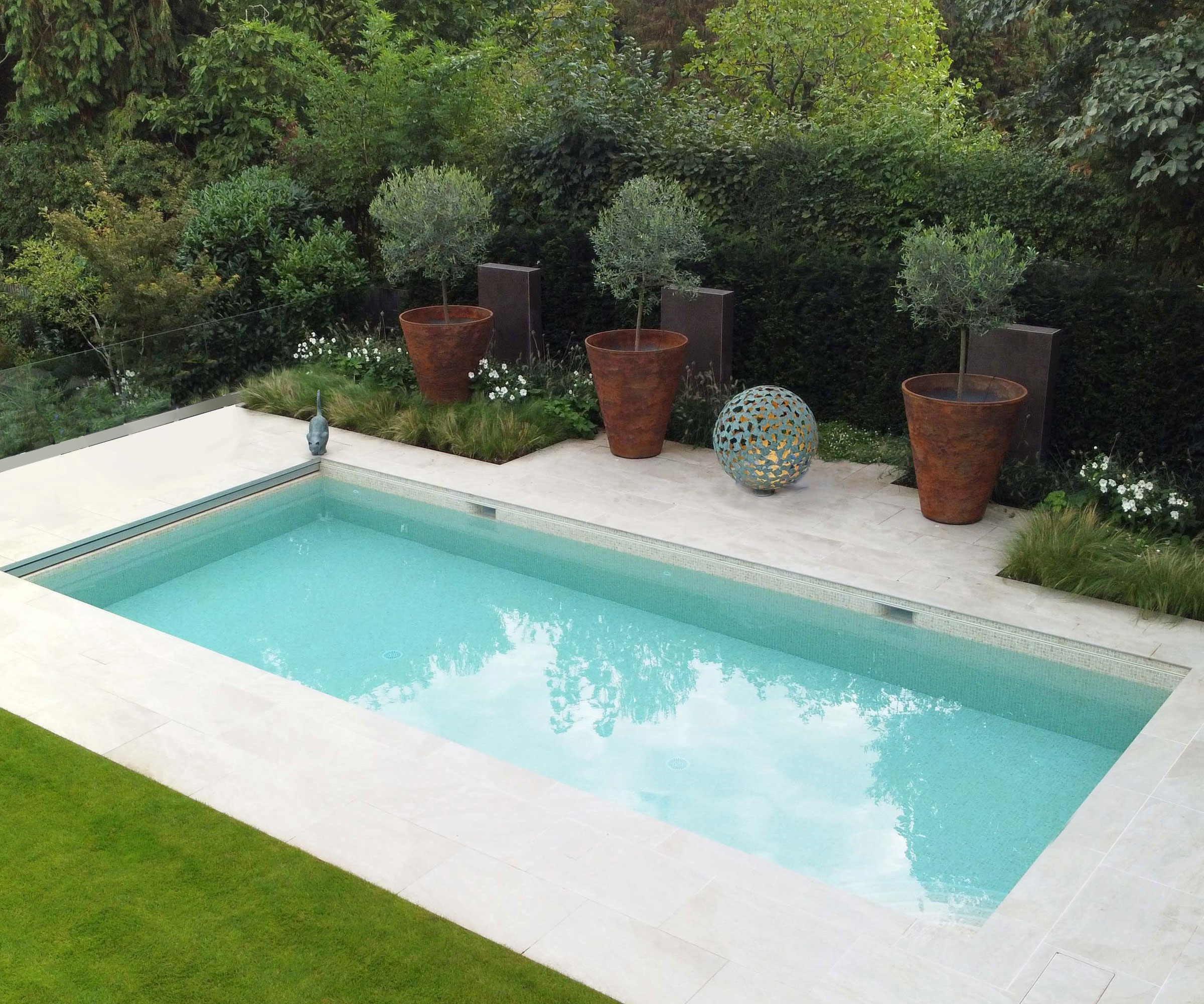 modern swimming pool design and patio surround with tall corten planters with topiary, surrounded by trees and shrubs