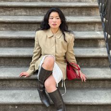 A woman sitting on the steps leading up to an apartment in a stylish outfit with a bouncy hairstyle