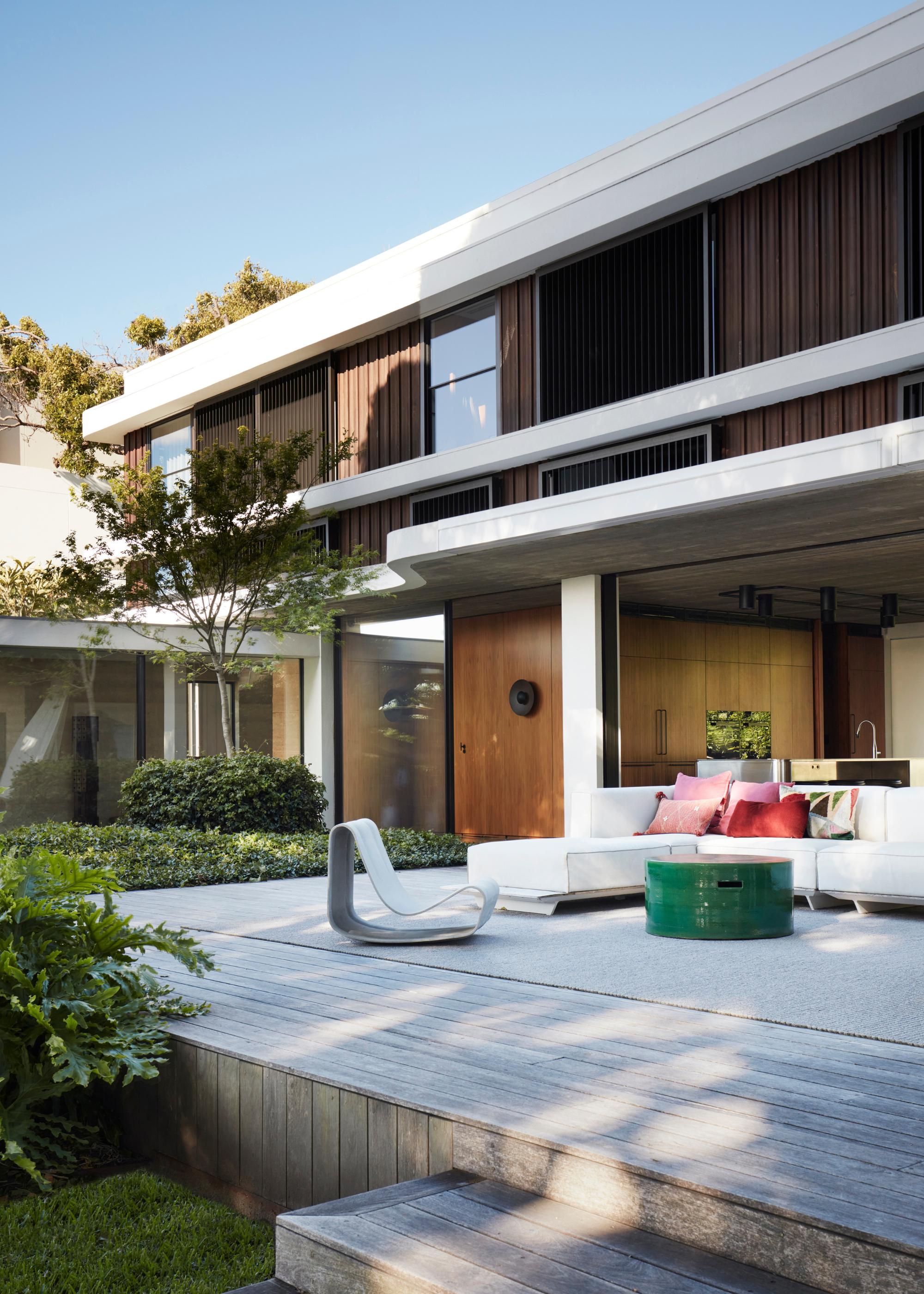A garden with an al fresco living area including a green side table, a structured chair and a sofa