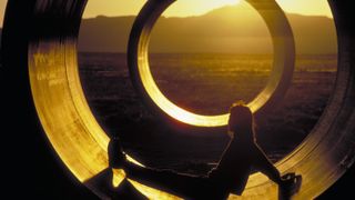 A person sits in the Sun Tunnels art installation in Utah as sunlet streams in through a hole