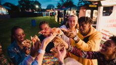 Group of young people sharing pizza in a field surrounded by food trucks