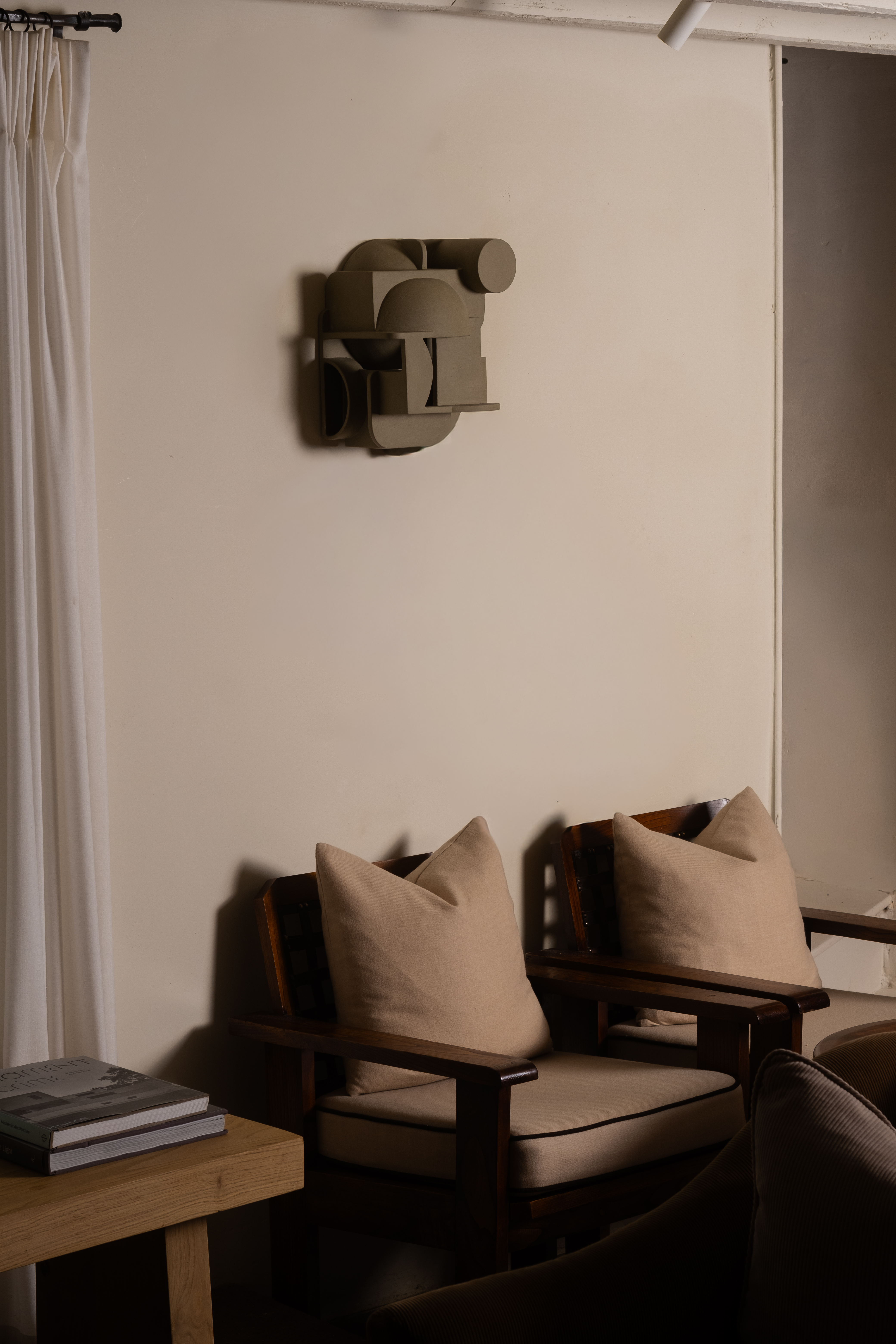 A multi-part, three-dimensional, abstract ceramic sculpture hangs on a beige wall in a modernly furnished hallway.