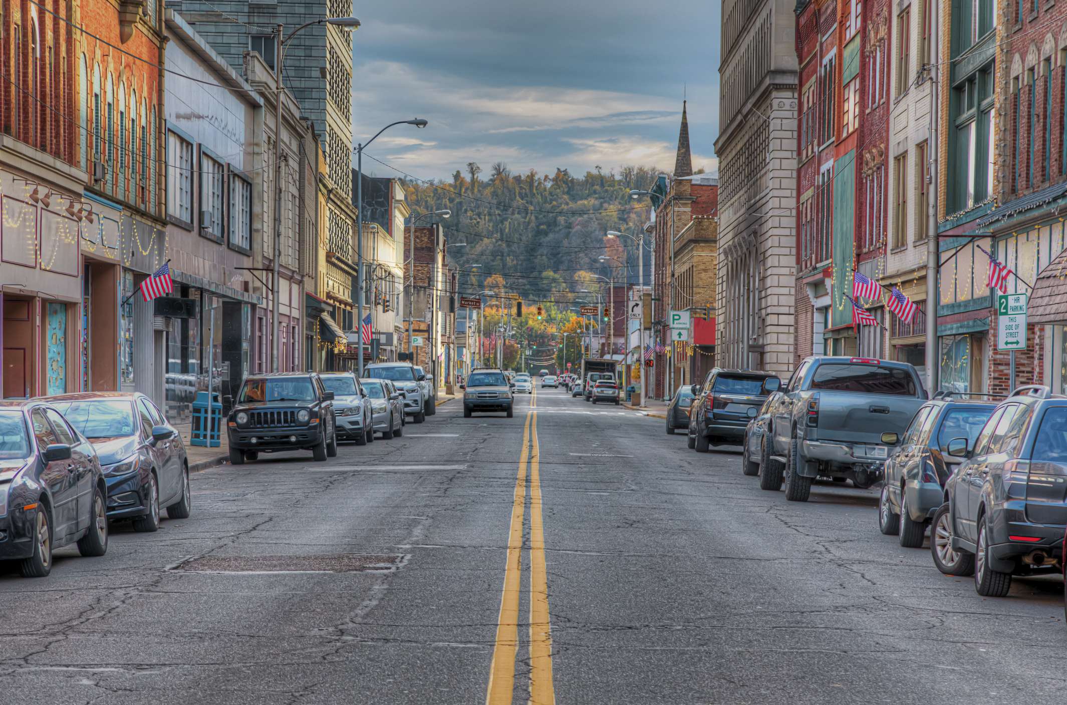Street view of Steubenville, Ohio, with tall buildings on either side and cars lining the road, with trees in the distance.