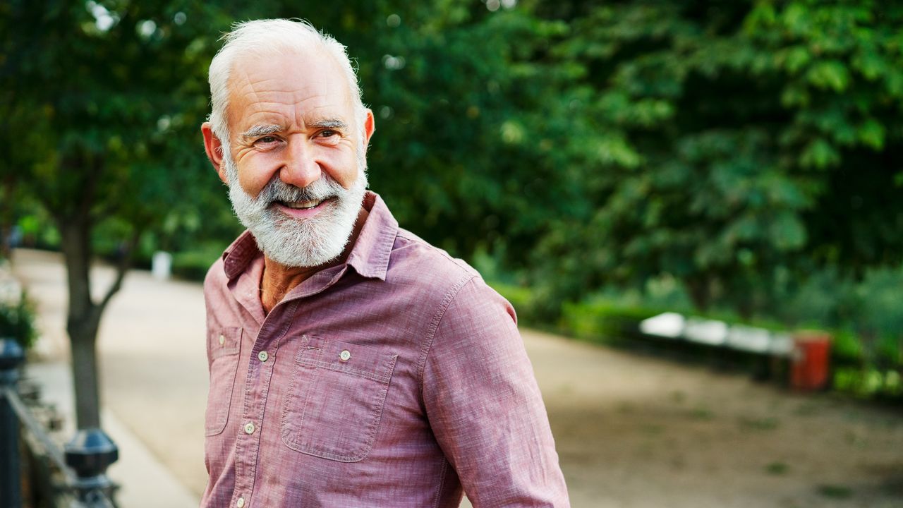 An older man smiles as he walks at a park.