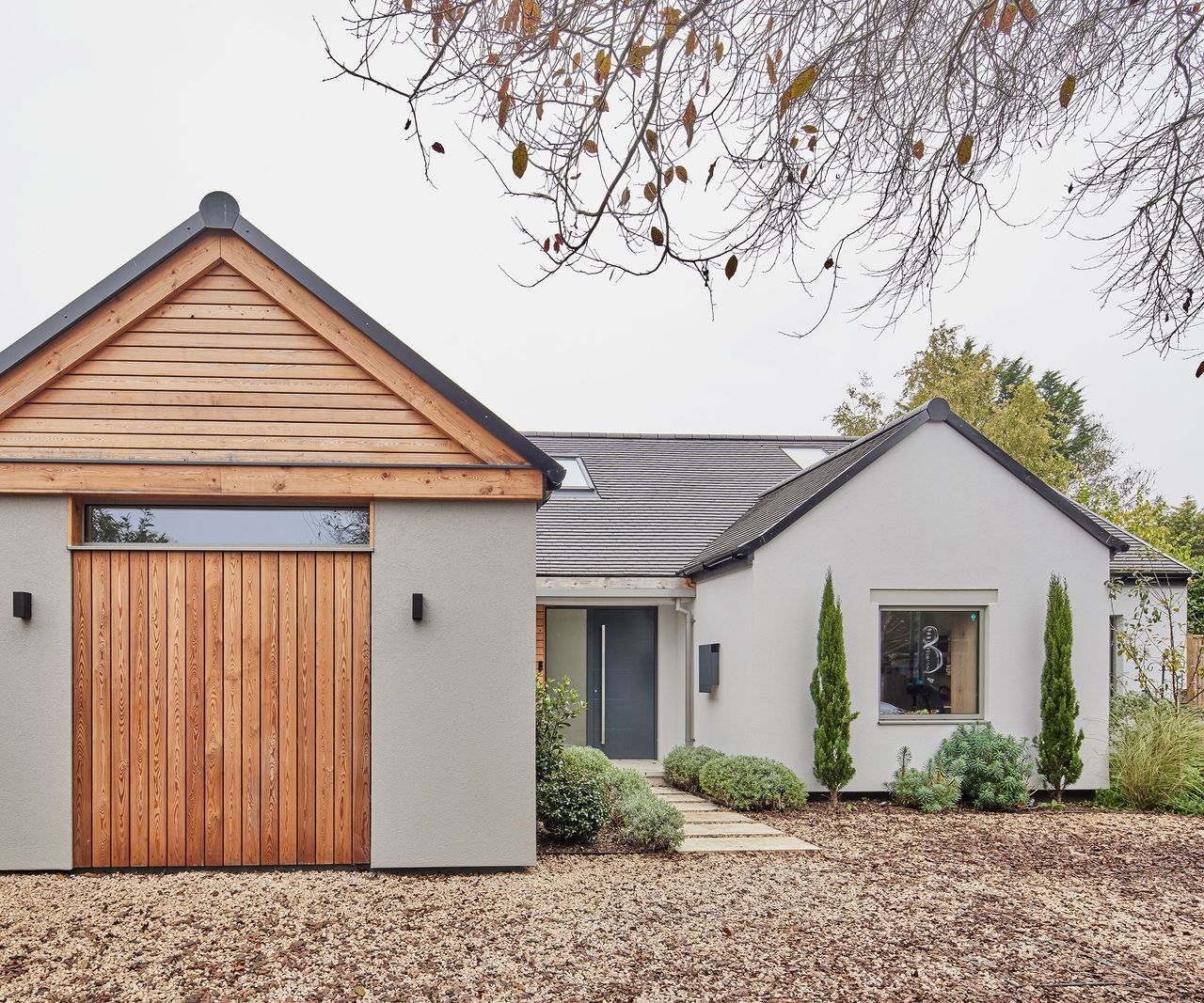 The front exterior of a new build home. The garage is clad in timber, and the rest is in a light render. The front garden and driveway is a gravel