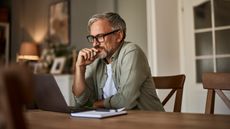 A man looks at his laptop while sitting at his dining room table.