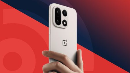 The OnePlus 15 being held in the hand on a red background