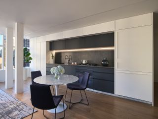 An open plan kitchen with a black slab cabinetry with under cabinet lights and a small round dining table