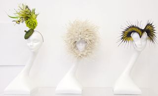 Left: Green hat with artificial foliage, a rose, and two butterflies. Middle: Fluffy cream hat which ties beneath the chin. Right: Yellow and black spikes protruding outwards and shaped onto the forehead