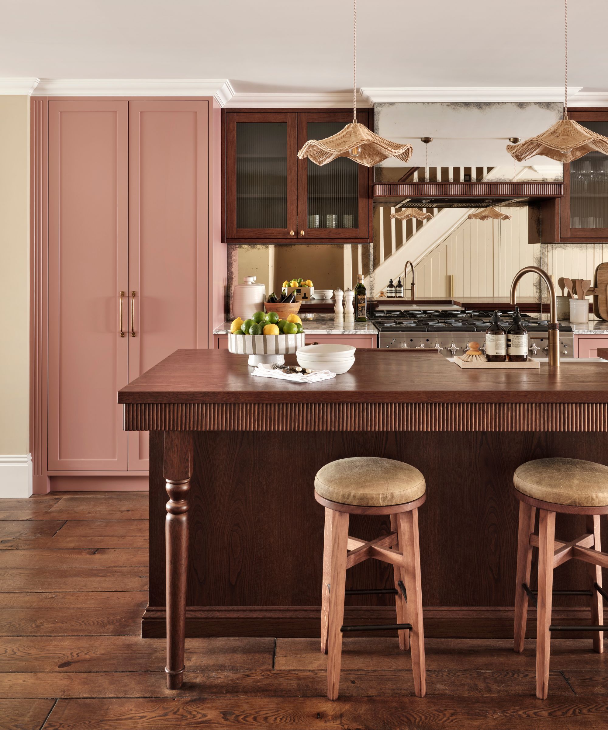 A kitchen with pink cabinets, a dark wood island, and rattan pendant lights