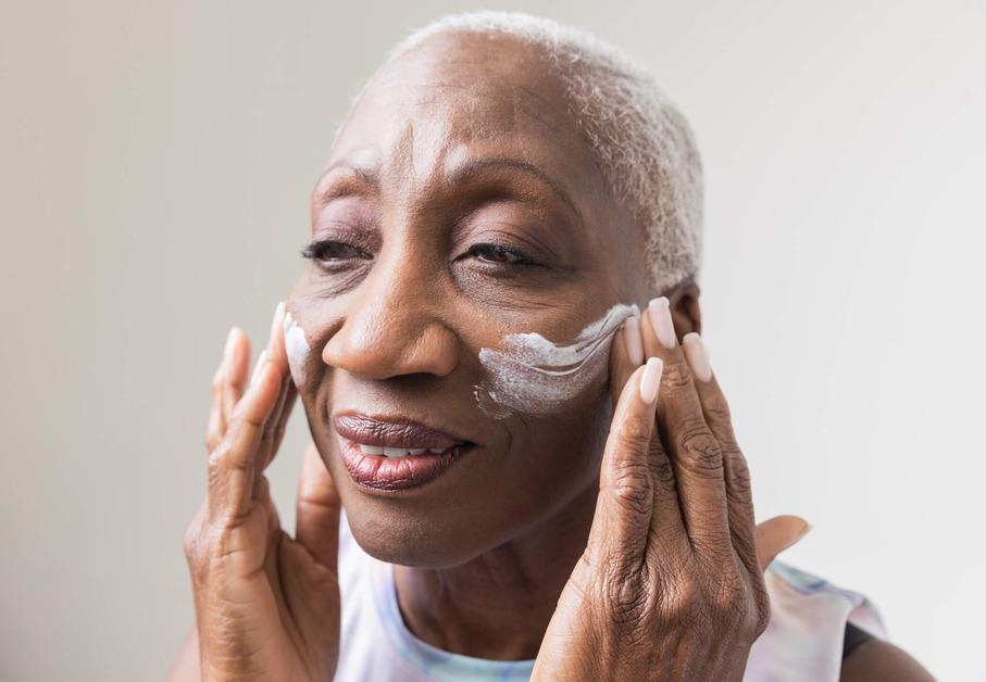  A mature black woman is applying moisturiser to her face.  