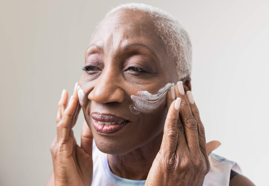 A mature black woman is applying moisturiser to her face. 