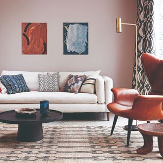 A pink-painted living room with a cream 4-seater sofa with five patterned cushions