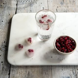 Gin glass with ice cube with pomegranate seeds.