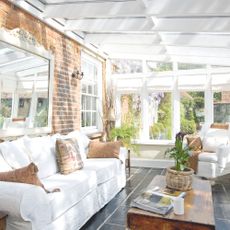 Light filled conservatory with light sofa and mirror on brick wall