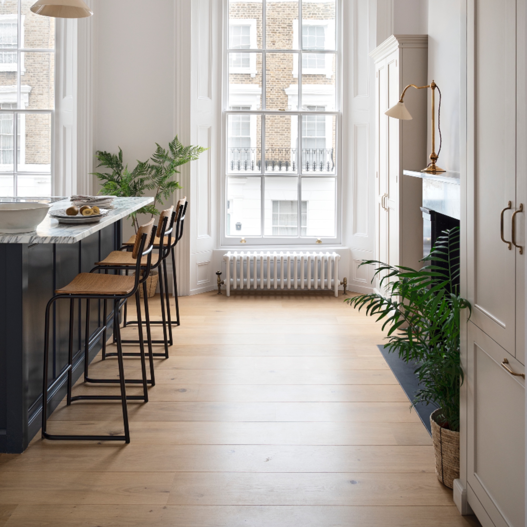white and marble kitchen, island with bar stools, wooden floor, freestanding storage cabinets