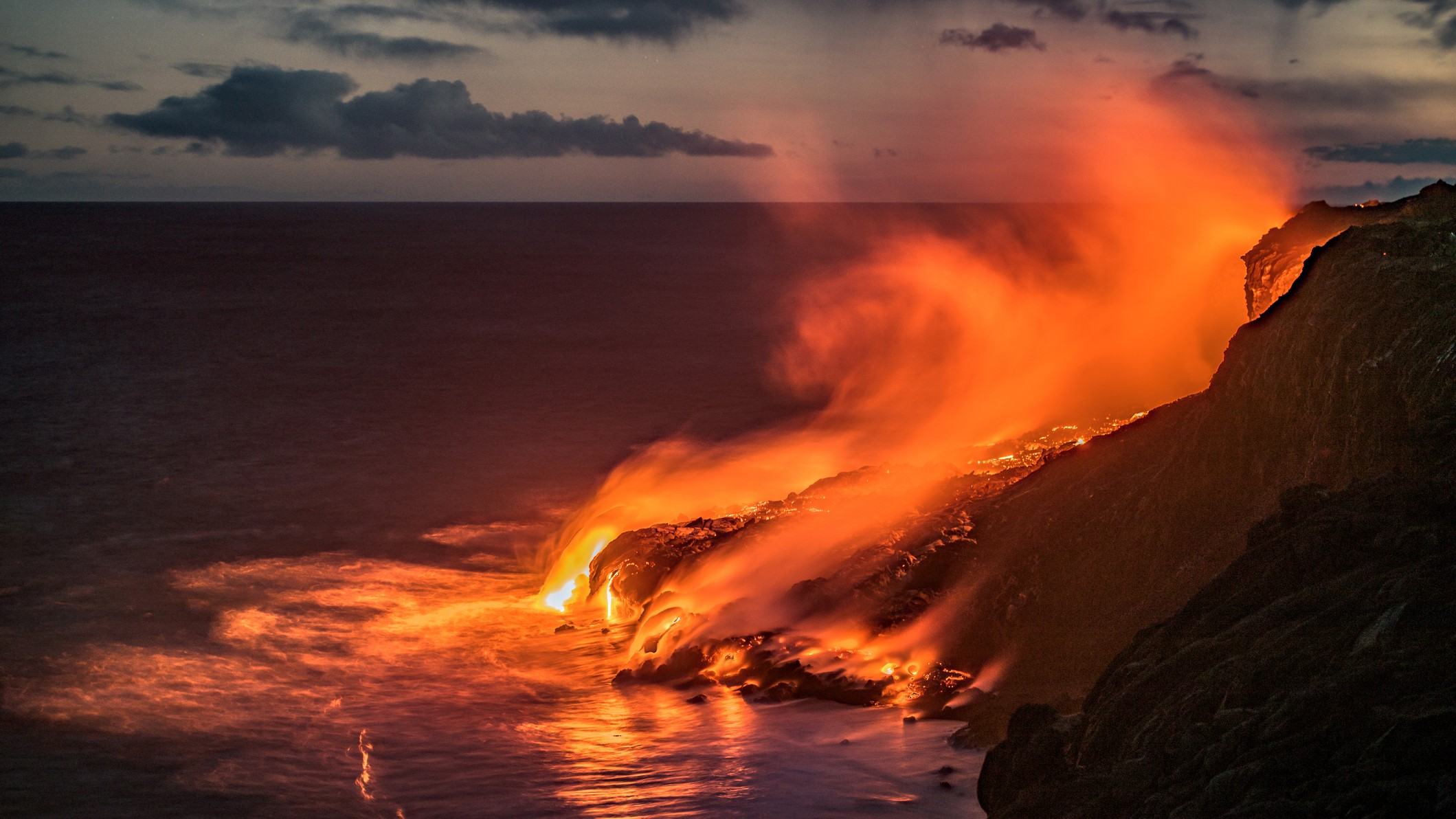 Lava cascades down to the ocean.