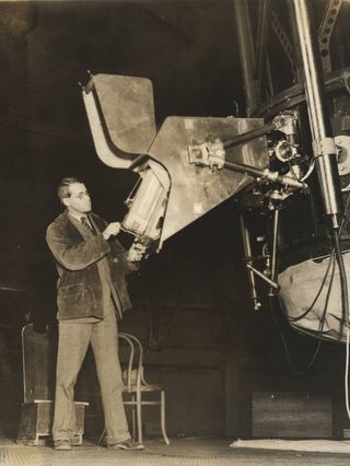 Paul W. Merrill standing at the spectrograph mounted on the 60-inch telescope at Mount Wilson Observatory.