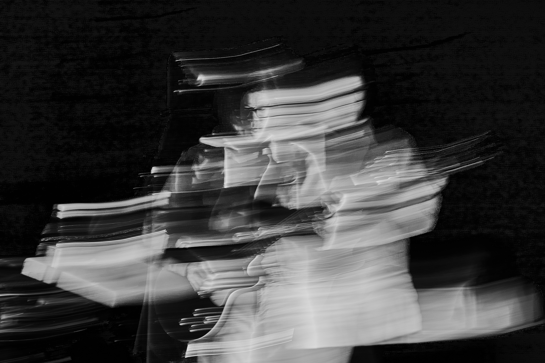 An abstract, long-exposure black-and-white photograph showing the motion blur of a figure playing an instrument against a dark background.