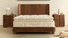 Avocado Grand Luxe mattress on a dark wood bed frame in a white bedroom with exposed brick walls and matching dark wood nightstands