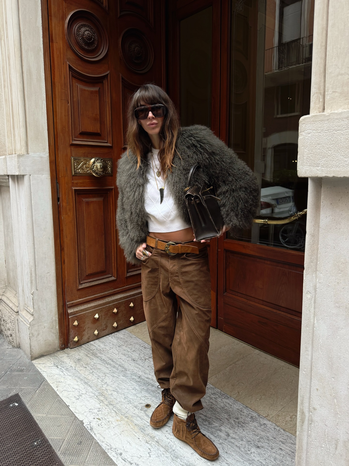 An image of an influencer in Paris wearing an olive-grey fur jacket with a white baby tee, brown cargo trousers, a brown leather belt and suede brown boots.