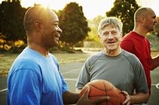 Three older men playing basketball and smiling.