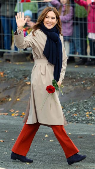 Queen Mary wearing red trousers, beige trench coat and thick black scarf