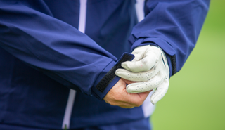 A golfer adjusts the wrist strap of the Proquip Darcey Ladies Rain Jacket