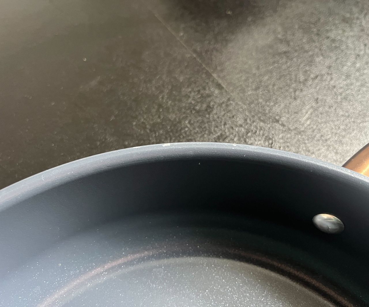 Slight peeling on the edge of a blue pan with a copper handle, on a black kitchen counter