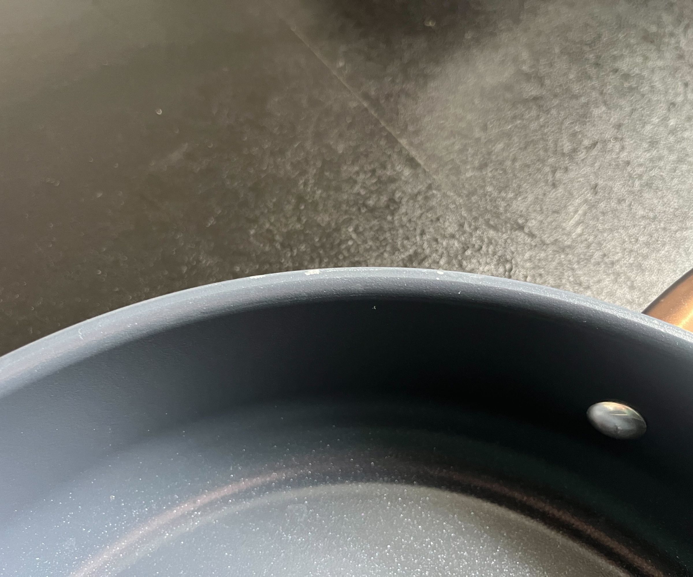 Slight peeling on the edge of a blue pan with a copper handle, on a black kitchen counter