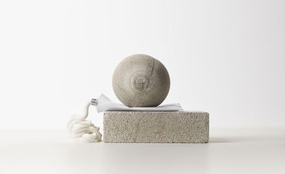 Concrete ball on top of concrete brick with tube of skincare squeezing out in between