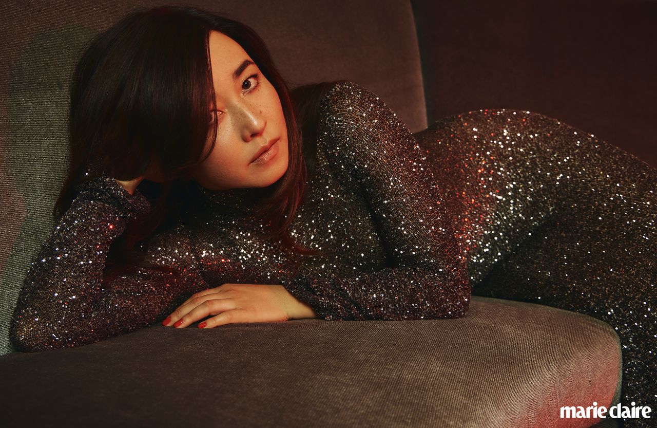 Actress Maya Erskine laying on a couch in a black sparkly dress